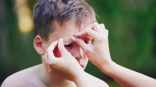 Applying Bandage to Boy's Forehead Outdoors