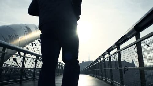 Silhouette of young man jogging on bridge in city in super slow motion