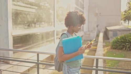 Smiling Woman Student Walks on Campus with Phone