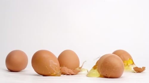 Brown eggs dropped and breaking on white studio backdrop in 4k slow motion