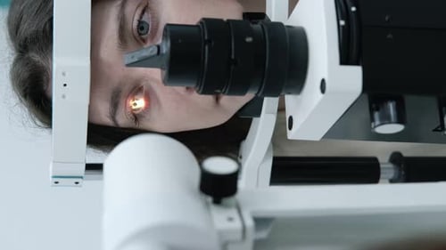 Attentive optometrist examining beautiful female patient with slit lamp in ophthalmology clinic. Opt