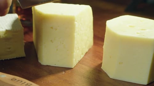 Three cheeses on cutting board, small knife cuts slice of Gouda block
