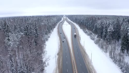 Top view of a passing bus, cars and truck on a highway in a snow-covered forest