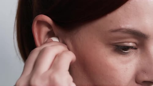 Woman Placing Wireless Earbud In Ear Close Up