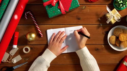 Writing Christmas List on Wooden Table Surrounded by Gifts