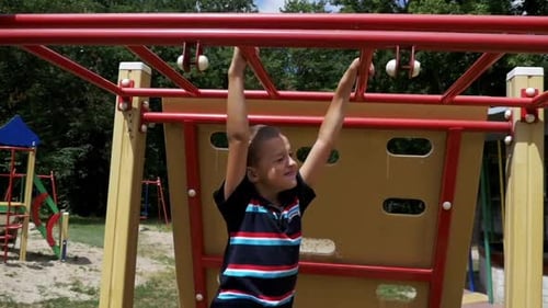 Young Boy Hang on Monkey Bars By His Hands to Exercise at Outdoor Playground Against the Sky in Slow