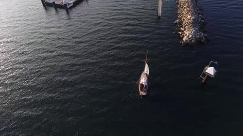 Sail boat reaching boat dock shore. Alone sail boat in the ocean, sail boat by the shore. Blue water