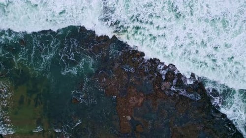 Aerial view foamy sea waves crashing by volcanic rocks in slow motion