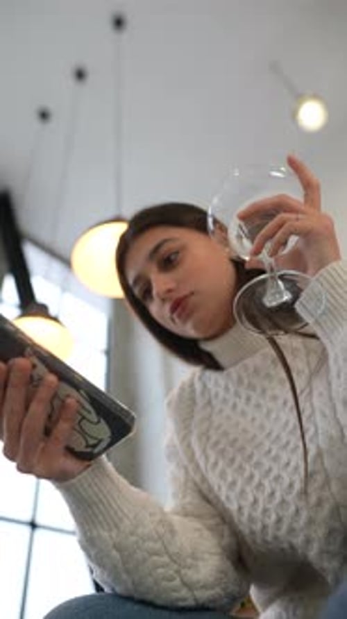 A Young Woman Sitting in a Cozy Cafe Enjoying a Relaxing Drink While Using Her Tablet