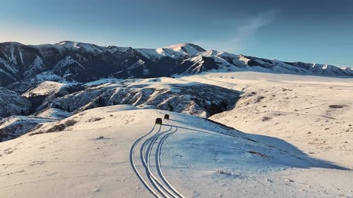 Vehicles Leaving Tracks on Snowy Mountain Ridge at Sunset