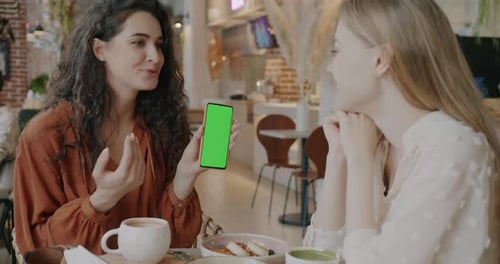 Happy Friends Looking at Smartphone with Chroma Key Green Screen and Talking Indoors in Cafe
