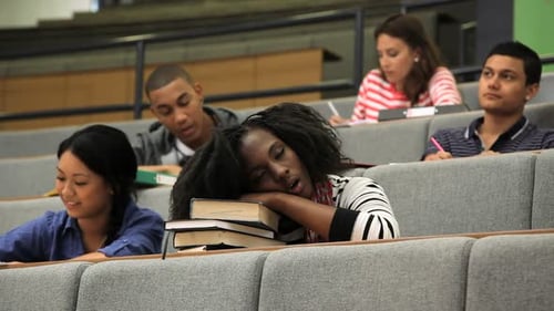 Female student falling asleep on books in lecture theatre, during class