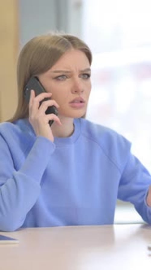 Upset Woman Talking on Phone at Table Indoors