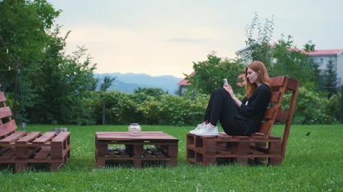 Beautiful Young Woman Enjoying the Sunset in Her Garden and Communicating on the Internet on a