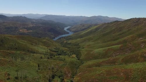 Drone View of River Meandering Through Rolling Green Hills on a Sunny Day