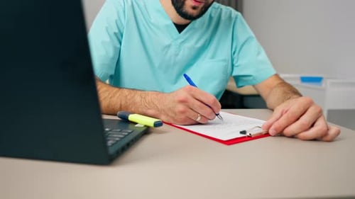 Close-up shot of a male doctor's hand with ring on his finger filling out a patient's history