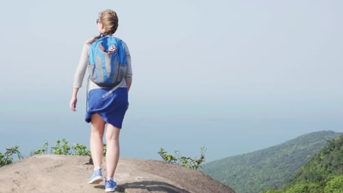Female tourist with backpack raising hands on top of mountain