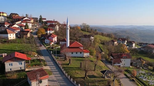 Aerial drone view of a picturesque hillside village featuring red roofed houses and a tall white mos