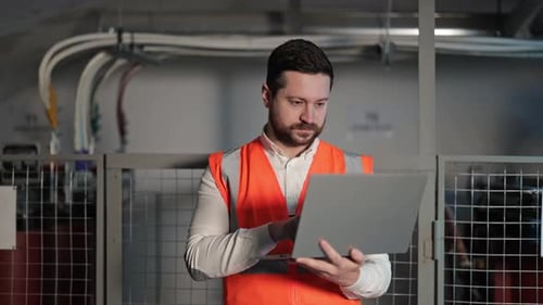 Electrical Engineer Using Laptop Next to Control Panel in Industrial Building