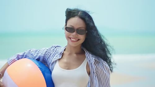 Slow motion of happy woman holding beach ball and smiling at camera