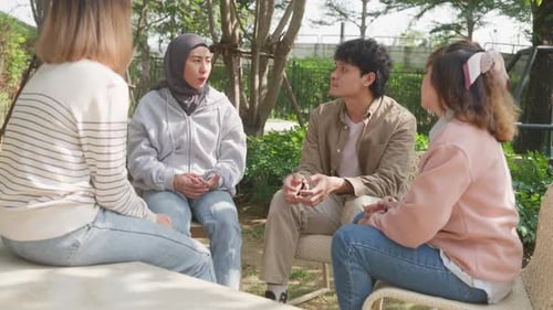 Small Asian group of people sit in a close circle and talk to a therapist in park.