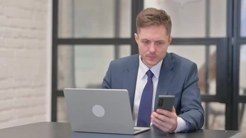 Man Using Laptop and Cell Phone at Desk