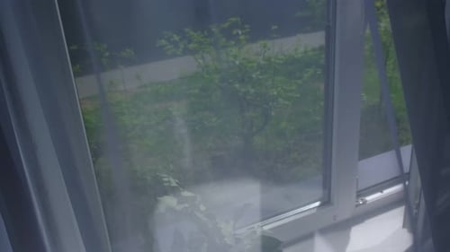 Le vent souffle à travers la fenêtre ouverte de la pièce en agitant du tulle blanc près de la fenêtre