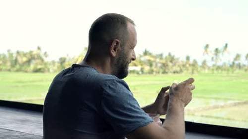 Young Man Playing Game on Smartphone in Cafe in Country 30s