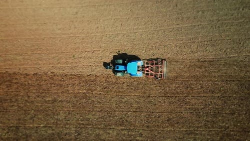 Aerial view of a tractor with harrow plowing a field before planting a crop.