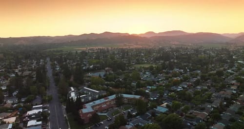 Flying over green city of Napa, California, USA. Mountainous skyline at backdrop of pink skies.