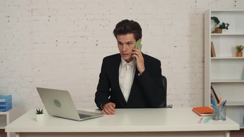 Medium Video of a Young Man Working on a Laptop in the Office Taking a Smartphone From the Table