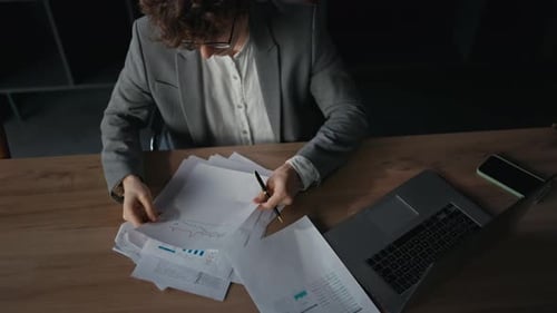 Nahaufnahme eines selbstbewussten jungen Mannes in einem grauen Anzug, der Dokumente und Arbeitsberichte untersucht, der an einem Tisch sitzt