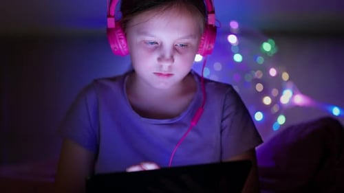 Girl Uses Tablet Wearing Headphones in Dark Room