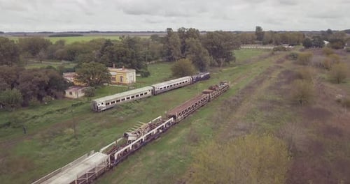 aerial view of an old train in motion with a rural school background and abandoned trains in,Buenos