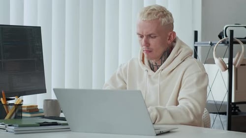 Tätowierter Entwickler analysiert Codierungsbildschirme auf Laptop und Computerbildschirm