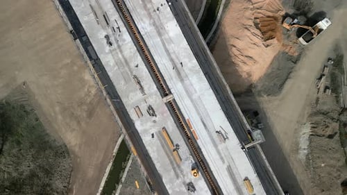 Vista de arriba hacia abajo de un puente en construcción que muestra los detalles de los trabajadores, los vehículos y los sitios circundantes