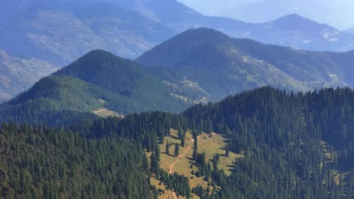 drone shot of of lush green forest covering rolling hills and distant mountains.