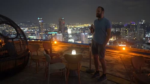 Handsome man enjoying tasty cocktail at luxurious rooftop bar at night