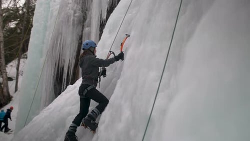 A woman climbing a frozen cliff face using ice axes