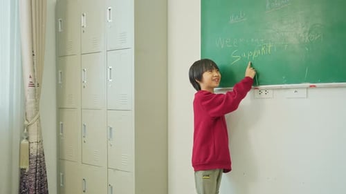 Young boy enjoy to write hir name on greenboard also spelling in front of classroom of home school.