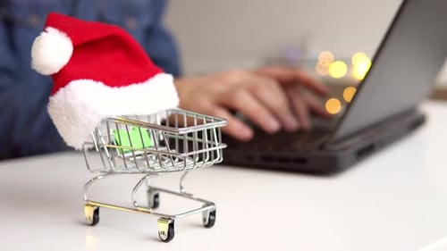 Festive Shopping Cart with Santa Hat near Laptop