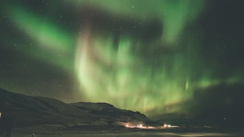 Timelapse of the aurora borealis moving over mountains and open fields in south Iceland