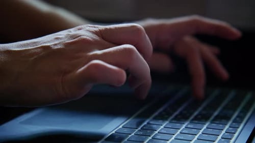 Hände, die während einer nächtlichen Arbeitssitzung zu Hause auf einer Laptoptastatur tippen
