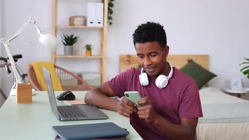 Young Adult Using Phone and Laptop at Desk