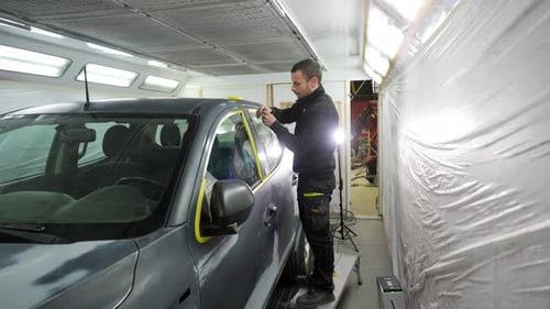 Professioneller Autolackierer, der vor dem Lackieren Klebeband anbringt