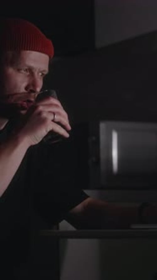 Side View of Man Sitting to Work at Laptop and Drinking Dark Beverage