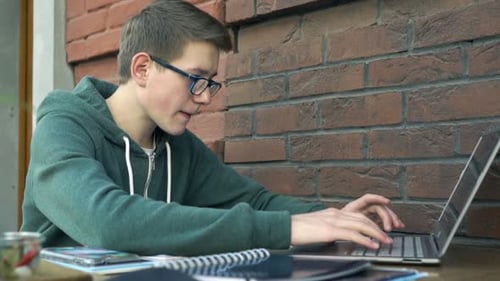 Teenager with Laptop and Notepad Doing Homework by Table in Cafe Adolescent