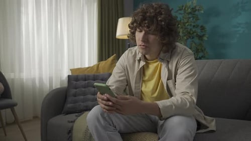 Young Adult Relaxing with Smartphone on Sofa Indoors