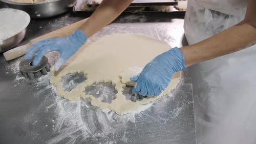 Baker Cutting Cookie Dough on a FlourDusted Stainless Steel Table
