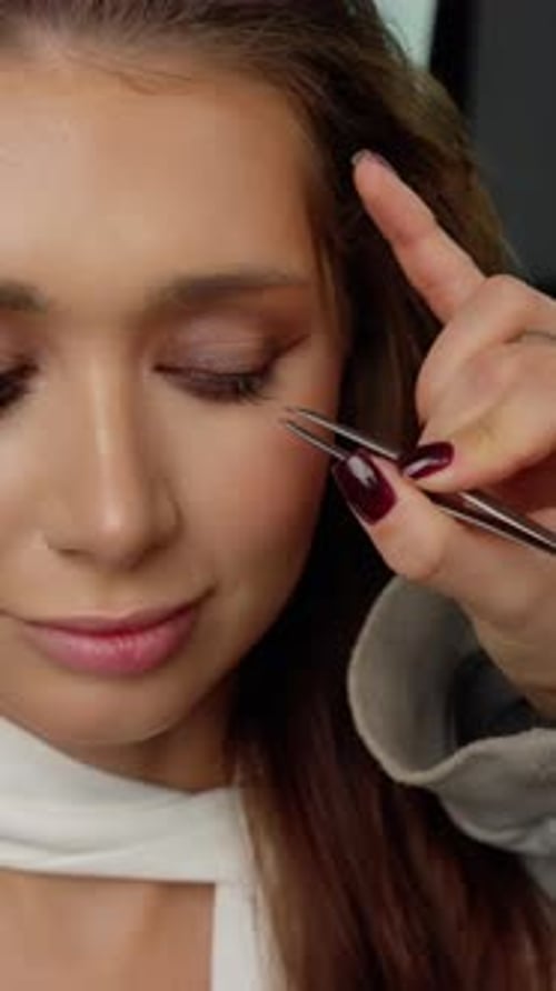 Professional Makeup Artist Applying False Eyelashes on Model's Eyelid with Precision Tweezers